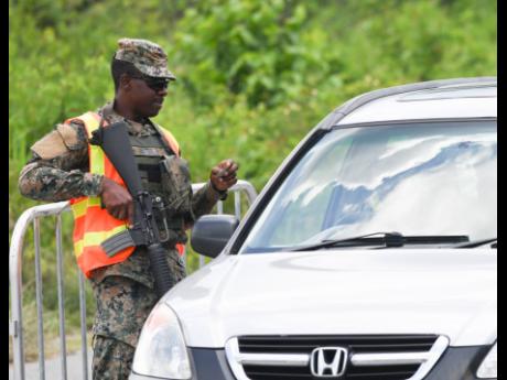 Credit: Ricardo Makyn A JDF member checks a driver’s licence in Whitehouse, Westmoreland, which is under a state of public emergency.