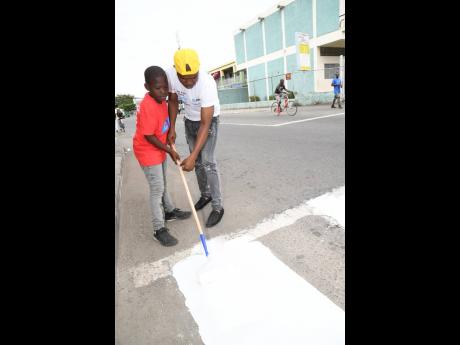 Jahmar Rose assists his son, Daniel, to paint a pedestrian crossing on the Gordon Town main road in St Andrew on Labour Day.