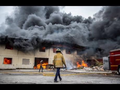 Members of the Jamaica Fire Brigade on the scene of the burning Auto Spares House on Upper Ivy Road, off Lyndhurst Road in St Andrew, yesterday. The huge blaze, fuelled by gusts of wind, also resulted in a homeowner counting her losses as the flames wreaked havoc on her dwelling.