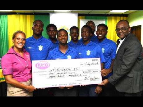 Credit: Ricardo Makyn Danielle Cunningham (left), beverage marketing manager, LASCO Distributors, presents a cheque for $1.2 million to Donovan White (right), president of the Waterhouse Football Club, at yesterday’s media briefing ahead of the Scotiabank Concacaf League match between Waterhouse and HS Herediano of Costa Rica. Sharing in the moment are Waterhouse head coach Marcel Gayle (fourth left) and several players of the club. The briefing was held at the offices of the Jamaica Football Federation.