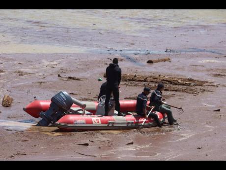A rescue boat navigates the muddy waters in the ongoing search. Below: Security forces gather to begin the search for victims of the bus crash.