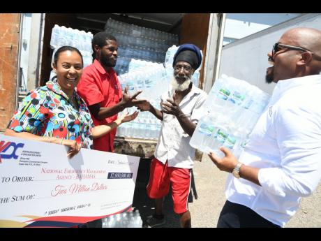 Alveta Knight, honorary consul for the The Bahamas to Jamaica, receives a cheque for $2 million and a truckload of water from Karl Tulloch (right), director of Kemtek Development and Construction Limited, while workmen unload the water at the Norman Manley International Airport in Kingston on Thursday, September 12, 2019. The donations were made to assist the people of The Bahamas who were recently affected by Hurricane Dorian, which hit the country earlier this month.