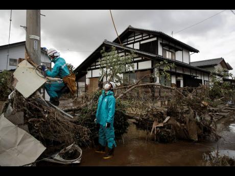 Electricity workers work in a neighborhood devastated by Typhoon Hagibis Tuesday, Oct. 15, 2019, in Nagano, Japan. More victims and more damage have been found in typhoon-hit areas of central and northern Japan, where rescue crews are searching for people still missing. (AP Photo/Jae C. Hong)