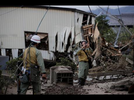 Workers survey damages in a neighborhood devastated by Typhoon Hagibis Tuesday, Oct. 15, 2019, in Nagano, Japan. More victims and more damage have been found in typhoon-hit areas of central and northern Japan, where rescue crews are searching for people still missing. (AP Photo/Jae C. Hong)