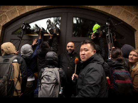 A private security guard (centre) stands as journalists film through the garage window of the home of former Nissan Chairman Carlos Ghosn in Beirut, Lebanon, yesterday.