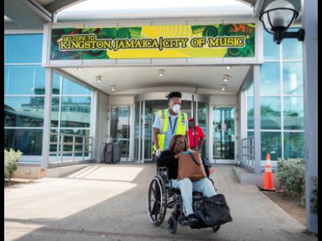 A worker is seen wearing gloves and a protective mask as he provides wheelchair assistance to an elderly traveller at the arrivals area of the Norman Manley International Airport on January 28, 2020. Business disruptions are inevitable, so prepare to weather the effects.