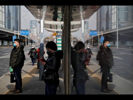 Commuters wearing protective face masks wait for buses at a stop in the Central Business District in Beijing, yesterday. 