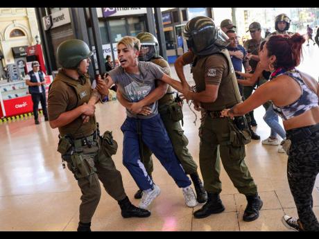 In this March 20 file photo, police detain two street vendors to evict them from the train station in Santiago, Chile, after the government ordered businesses to close and street vendors to go home as a precaution against the spread of the new coronavirus. 