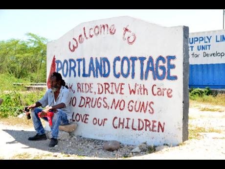 Abraham Gullivan awaits a taxi on Thursday while sitting in front of the sign welcoming commuters to Portland Cottage, a Clarendon community which is of major concern for health officials tracking COVID-19 in Jamaica. 