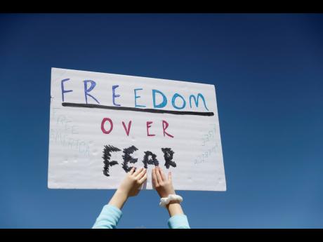 In this April 21, 2020  photo, a person holds a sign while gathering with others to protest stay-at-home orders put into place due to the COVID-19 outbreak outside the Missouri Capitol in Jefferson City, Missouri.