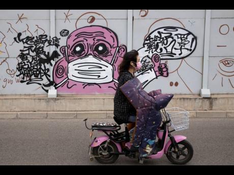 A woman wearing a mask against the coronavirus rides past graffiti with the words “Wear your mask properly” in Beijing on Friday, May 15, 2020.
