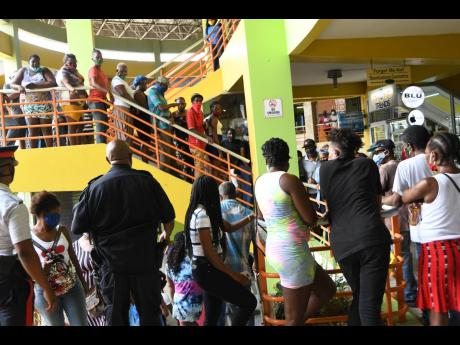Police officers try to create social distancing between scores of people who gathered at the Western Union outlet at the Pavilion Mall to collect the compassionate grant issued by the Government.