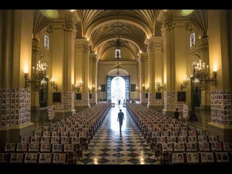 A man walks among portraits of people who died due to the COVID-19, inside the Cathedral in Lima, Peru, on Saturday.
