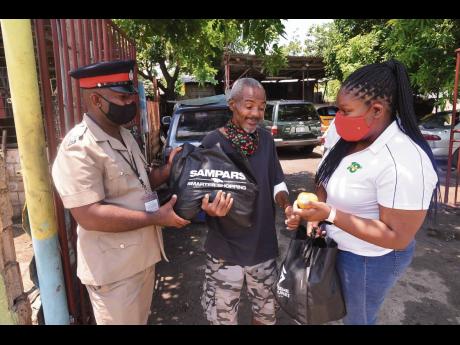 Roderick Brown (left), inspector at Gregory Park Police Station, and Kajay Rowe (right), digital and social media manager at Supreme Ventures Limited, share a light-hearted conversation with Orlando Cohen as he collects care packages in Gregory Park, St Ca