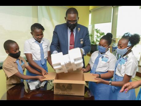 Principal of Golden Spring Primary School Winston Smith is assisted by his delighted students (from left) Minnell Nagent, Arianna Jones, Kadija Worghs and Celina Brignhy to unwrap and test the new multipurpose projector received from the NCB Foundation to 