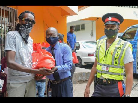 NCB’s Gratitude Bus was on the move with the support of members of the Jamaica Constabulary Force. Here, NCB’s Devon Wilson (centre) hands over a care package to a resident of the Mount James community in Stony Hill, St Andrew, during a recent visit to
