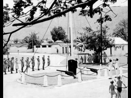 The commander of the Caribbean area, Brigadier Derek Lister, and members of the Staff and Services of the Headquarters Caribbean Area saluting the Union Jack as it was slowly lowered for the last time, while two buglers of the Jamaica Regiment sounded the 