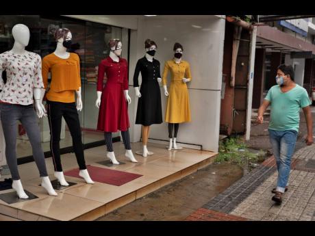 A man wearing a mask as a precaution against the coronavirus walks past mannequins displayed with masks outside a clothing store in Kochi, Kerala, India.