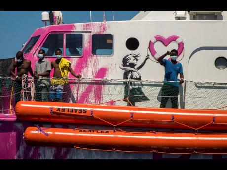 A boy waves from the deck of the ‘Louise Michel’ rescue vessel, a former French patrol boat currently manned by activists and funded by the renowned artist Banksy, in the Central Mediterranean Sea, 50 miles south from Lampedusa, Italy, on Friday, Augu