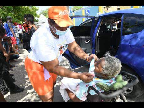 Credit: Rudolph Brown Alecia Dicks (left) places a mask on Cynthia Gallimore before she casts her vote at the Whitfield All age school in the St. Andrew South West constituency.