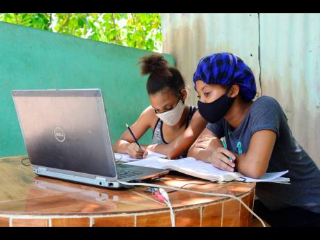 Credit: Nicholas Nunes/Photographer
Two students of The Queen’s School accessing classes using a laptop under an ackee tree on Mountain View Avenue in Kingston last Wednesday. One of the girls had slept over at her classmate’s house so they could have classes together.