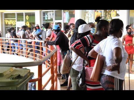 In this May 2020 photo a long line is seein in Pavillion Mall in Half Way Tree, people were waiting to collect their Compassionate Care Grant paid out by the government via Western Union. Social distancing, sanitising and wearing of masks are critical in s