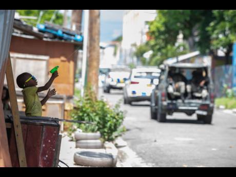 A boy plays with a water gun as a convoy of vehicles with police and soldiers passed by on Fleet Street on Sunday. Paradise Gardens was placed under a curfew late Friday as a countermeasure to increased crime in the community.