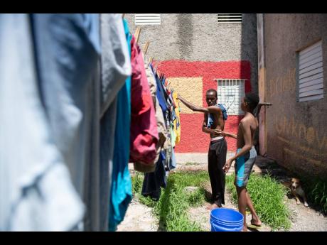Linval Rogers, a resident of Parade Gardens, hangs out laundry on Sunday, October 11. Rogers is assisted by his nephew, Christopher Burton, and has no complaints about the curfew imposed on the community.