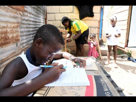 Credit: Rudolph Brown/Photographer Trench Town resident Nekesha Gayle checks up on progress being made by a student. The 37-year-old volunteers to help students stay engaged with online classes in the community. In the foreground, Terrick Petgrave completes an assignment.