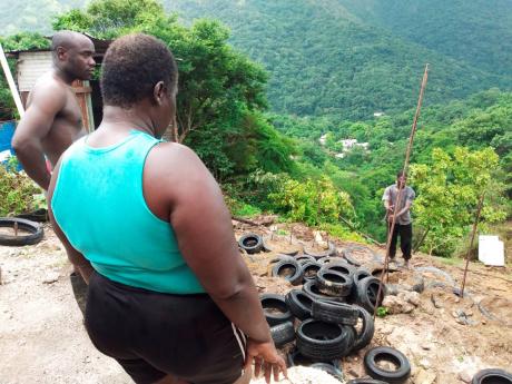 Gaylia Catwell watches as a workman sets out tyres and steel in a makeshift bid to shore up her backyard and the foundation of her house in Lindo’s Gap, St Andrew East Rural, last Thursday. 