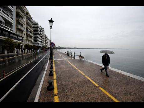 A pedestrian holds an umbrella as he walks on a coastal avenue during the lockdown to contain the spread of COVID-19 in the northern city of Thessaloniki, Greece, Tuesday, November 3, 2020. Greece’s government imposed a localised lockdown on its second l