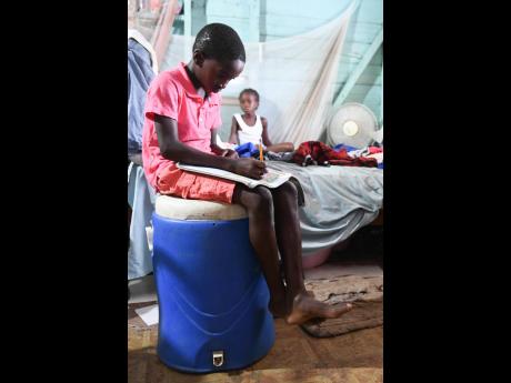 Credit: Joel Young reads while sitting on a cool box close to the bed in his family house in Little Bay, a mainly fishing community located in the parish of Westmoreland, the western end of the island of Jamaica. Joel doesn’t have a table in the house.