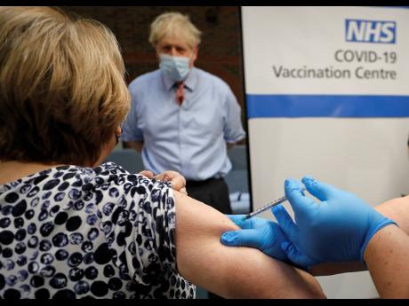 British Prime Minister Boris Johnson watches as nurse Rebecca Cathersides administers the Pfizer-BioNTech COVID-19 vaccine to Lyn Wheeler at Guy’s Hospital in London on Tuesday, December 8. UK health authorities rolled out the first doses of a widely tes