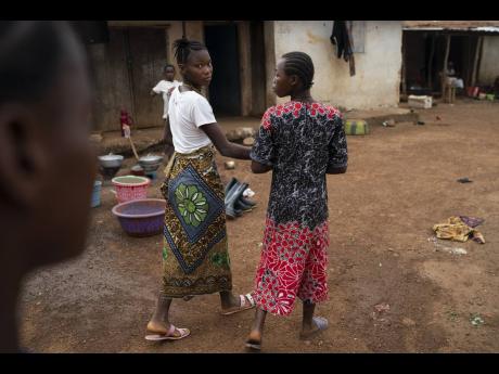 Marie walks with a friend on a street in Komao village, on the outskirts of Koidu, district of Kono, Sierra Leone, in November.