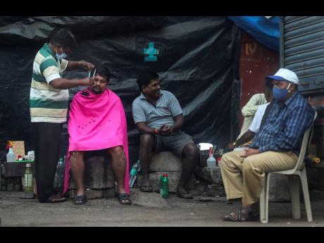 A roadside barber wearing a face mask as a precaution against the coronavirus, gives a haircut to a man as others wait for their turn, in Mumbai, India, on Sunday, January 3. India authorised two COVID-19 vaccines on Sunday, paving the way for a huge inocu