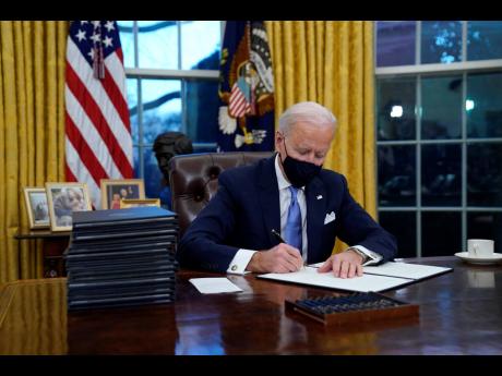 Credit: AP President Joe Biden signs his first executive order in the Oval Office of the White House on Wednesday, January 20, in Washington.