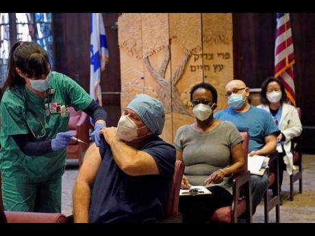 In this December 30, 2020 file photo, nurse manager Rob Treiber receives a COVID-19 vaccine at Hebrew Rehabilitation Center in Boston. Nearly a year to the day after Wuhan went into lockdown to contain a virus that had already escaped, President Joe Biden 