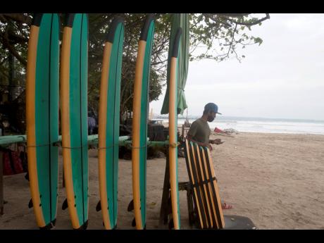 A man stands next to his surfboard stall as he waits for a costumer at a beach in Bali, Indonesia, on Wednesday, February 3. Amid fears of new variants of the virus, new restrictions on movement have hit just as people start to look ahead to what is usuall