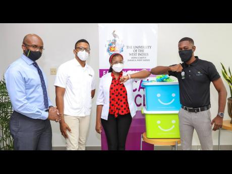 Fabian Gordon (right), financial adviser, Sagicor Life Jamaica, shares the customary elbow bump greeting with Thea Quaccoo (second right), fourth- year medical sciences student at The University of the West Indies (UWI), following the handover of personal 