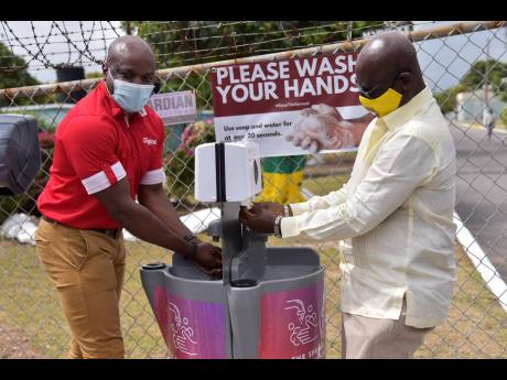 Local Government and Rural Development Minister Desmond McKenzie (right) and Public Relations and Communications Manager Digicel Jamaica, Elon Parkinson, use one of the handwashing stations provided by Digicel Jamaica to safeguard the health of homeless an