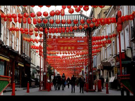 
People walk beneath lanterns hung across the street to celebrate the Chinese Lunar New Year which marks the Year of the Ox, in the Chinatown district of central London, Friday, February 12, 2021. 