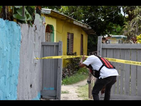 An investigator enters the yard where 24-year-old Cody McLaughlin was gunned down in Duncans Pen, St Catherine.