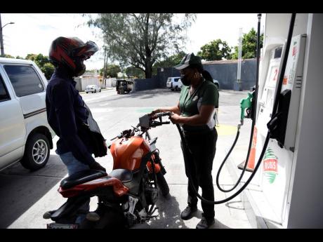 A motorcyclist watches as an attendant pumps petrol at a RUBiS service station in Vineyard Town, Kingston.