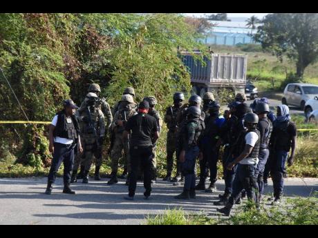 Policemen and soldiers gather to search a heavily vegetated section along the Spanish Town Bypass where four robbers who targeted a credit union in Portmore escaped after abandoning a Nissan Latio motor car.