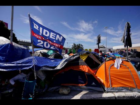 A donated campaign flag for US President Joe Biden flies over tents at a makeshift camp of migrants at the border port of entry leading to the United States on Wednesday, March 17, 2021, in Tijuana, Mexico. The migrant camp shows how confusion has undercut