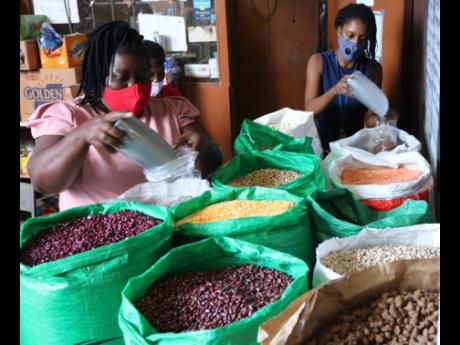Proprietor of Quality Grains, Sylvia Tomlinson-Hird (left), steps in to serve a customer during a busy period at her business place at 99 Newport Boulevard, St Andrew, on Thursday.