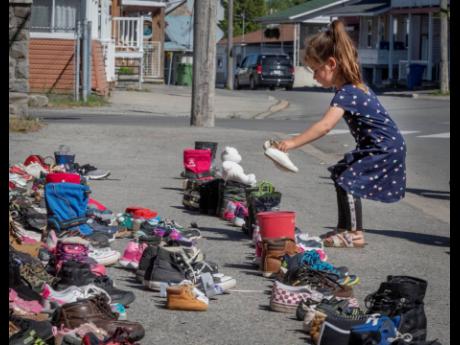 A four-year-old girl places a pair of her own shoes in front of the St Francis Xavier Church in Kahnawake, Quebec, on Saturday, as a memorial to the 215 children whose remains have been found buried at the site of a former residential school in Kamloops.