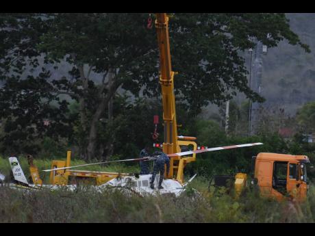 Credit: Kenyon Hemans/Photographer Jamaica Defence Force personnel attaching the helicopter to a crane for it to be lifted on to the back of a flatbed truck for transportation to Kingston after the student-flown aircraft landed in a farm in Dunbeholden, St Catherine, yesterday. No serious i