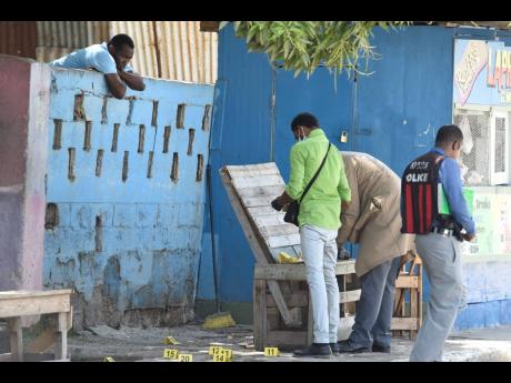 Credit: Nicholas Nunes/Photographer A resident of Third Street, Trench Town, looks over a wall as investigators process a crime scene where Laphane Bent was murdered on Tuesday morning.