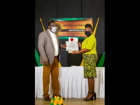 Cassandra Nicole Beach-Davis, one of 37 newly commissioned justices of the peace, accepts her instrument of appointment from the Rev Hartley Perrin, custos of Westmoreland.